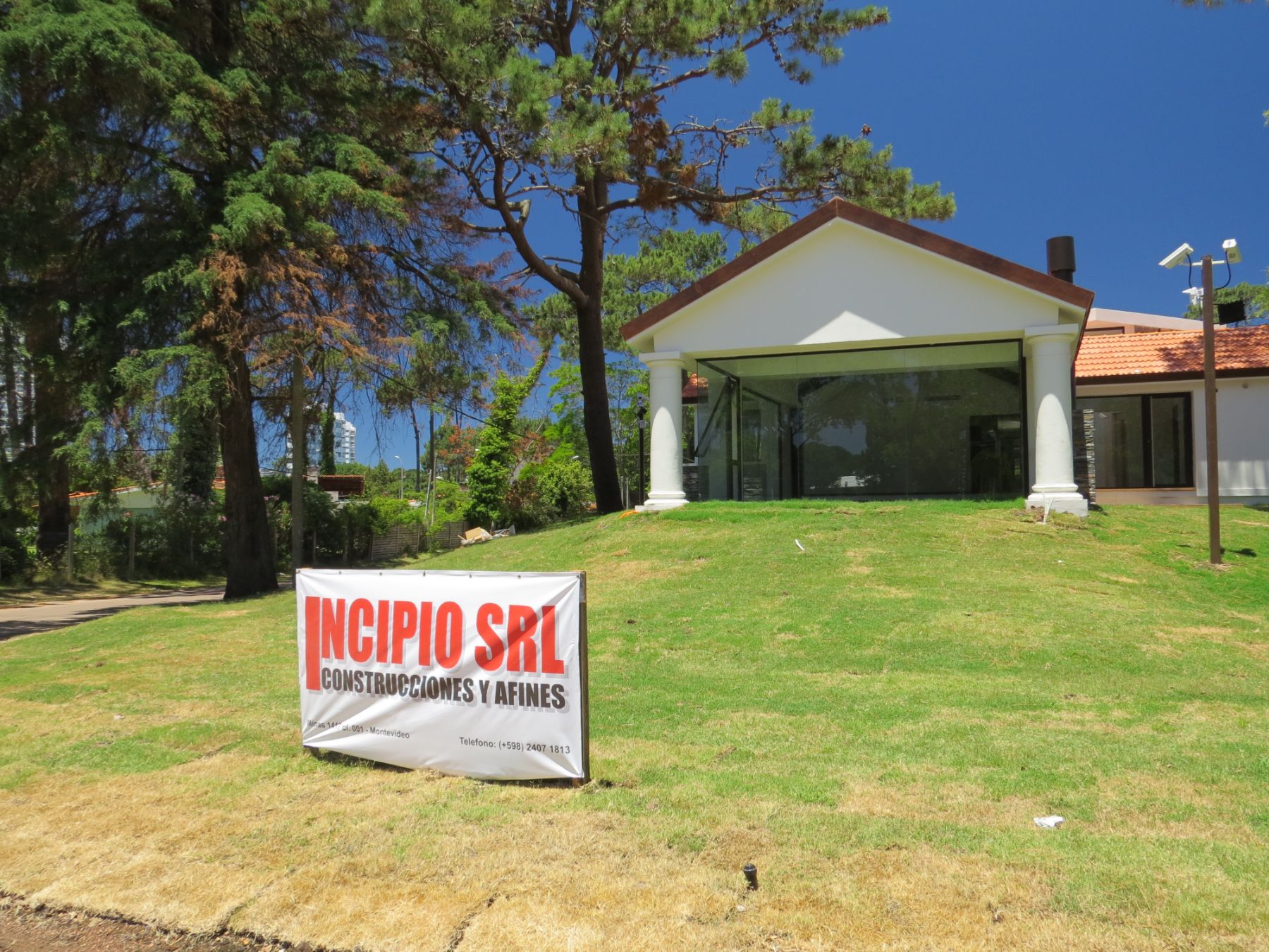La imágen es una fotografía tomada desde la proa de la clínica de blue cross de punta del este. En la misma se ve un ventanal enmarcado en dos columnas redondas, sobre las que descansa un tejado a dos aguas. Todo esto apollado sobre una colina.